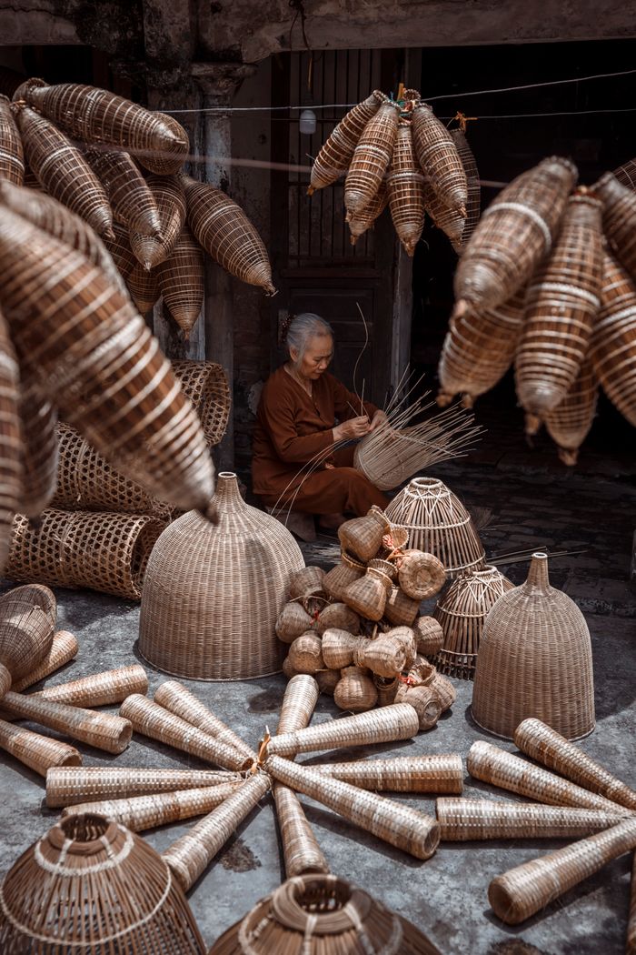 A woman skillfully weaving baskets in an outdoor Asian market, showcasing cultural craftsmanship.